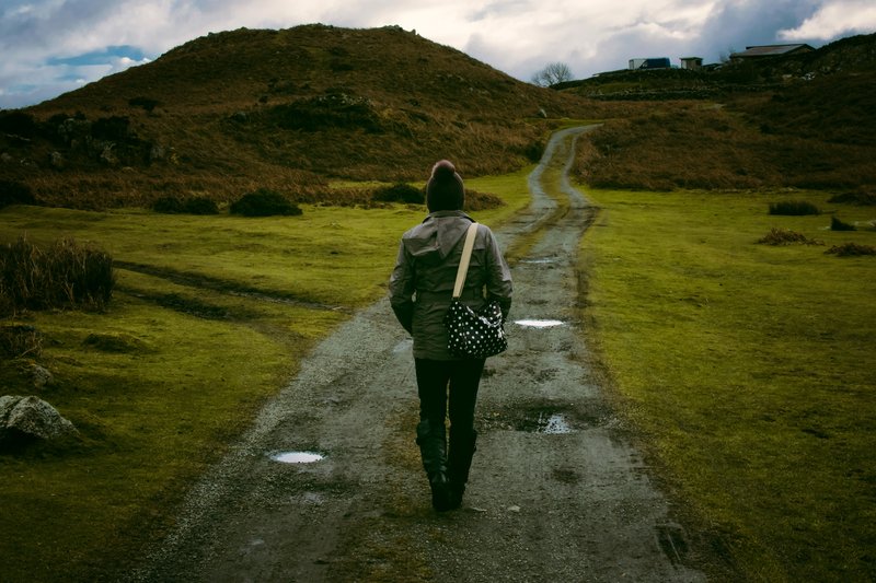 Person walking down a path toward a hill carrying a bag. 